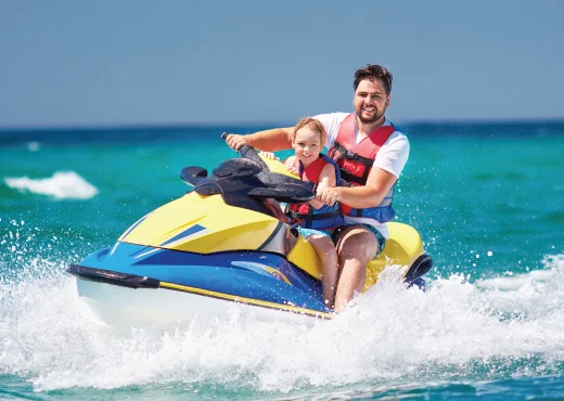 father and young son smiling as they ride a jet ski on a clear lake