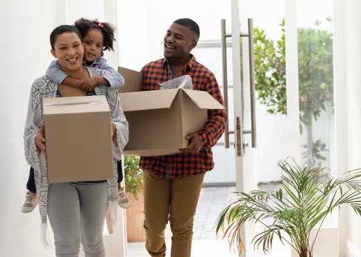 family with young daughter smiling as they move boxes into their new home