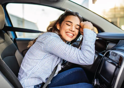 young female driver hugging the steering wheel of her newly purchased car