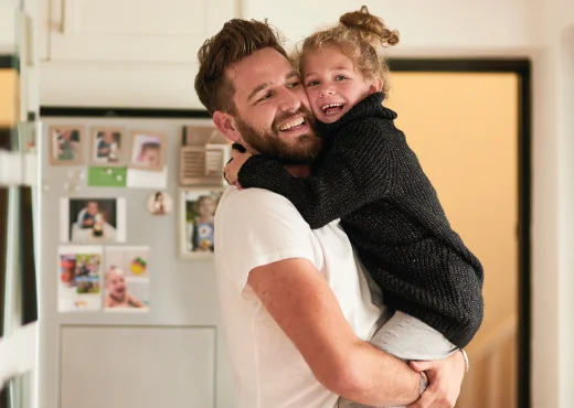 father carrying young daughter in his arms standing in their home kitchen