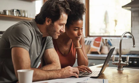 adult couple in kitchen looking at laptop planning a major purchase